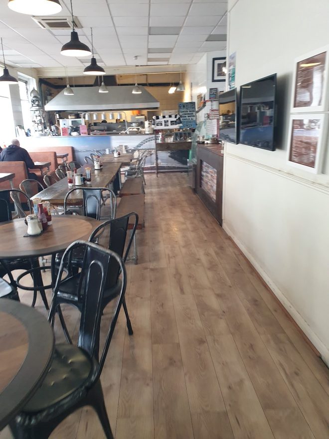 Along the wooden floor past tables and chairs towards the counter side of the room