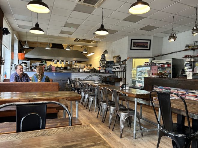 Long wooden tables and black chairs facing the service counter